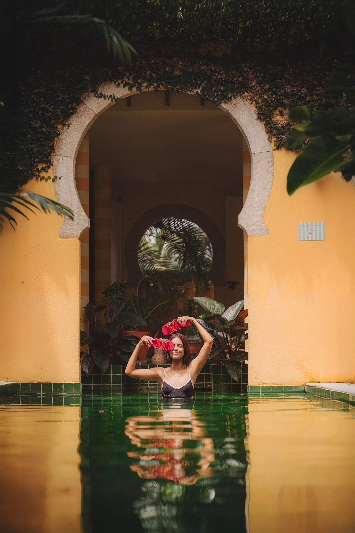lugar iluminado pelo sol, com piscina e uma mulher segurando sandálias de couro com design autoral 